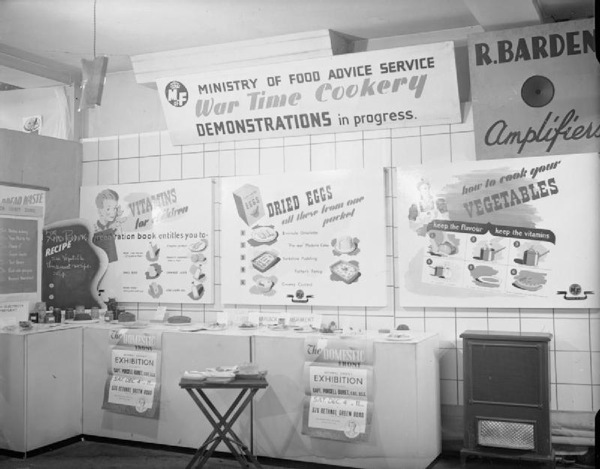 A view of a display by the Ministry of Food at the 'Domestic Front' exhibition held at James Brooke and Sons Ltd., 376 Bethnal Green Road. This display focuses on wartime cookery demonstrations and includes information on vitamins, dried eggs and vegetables.